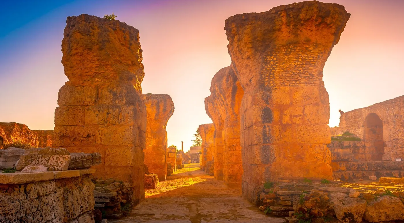 The ruins of Carthage lit gold at sunset, with broken stone walls standing against the sky
