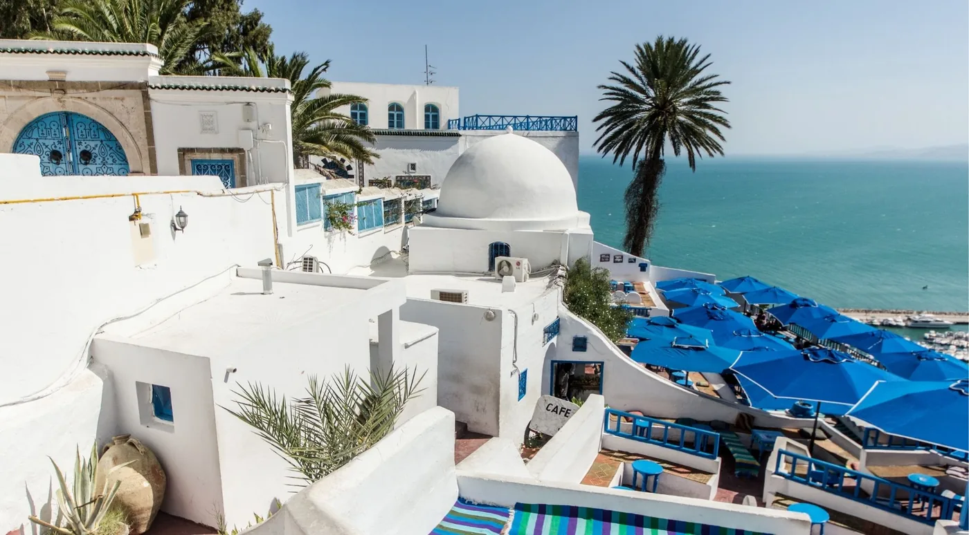 Sidi Bou Said rooftops with blue parasols, a white dome and the Mediterranean beyond