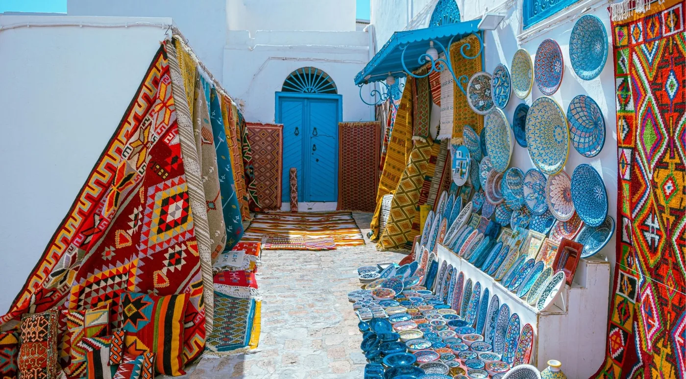 Carpets and painted ceramic plates hung along a narrow Sidi Bou Said street