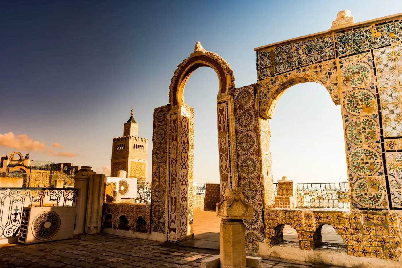 A tiled horseshoe arch on a medina rooftop at sunset, Tunis