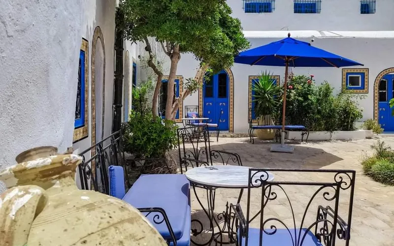 Whitewashed courtyard with blue doors and a blue parasol at Hôtel Bou Fares in Sidi Bou Said